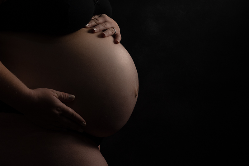 Photo de grossesse réalisée par Céline Gardé et représentant un joli ventre rond en gros plan sur fond noir.