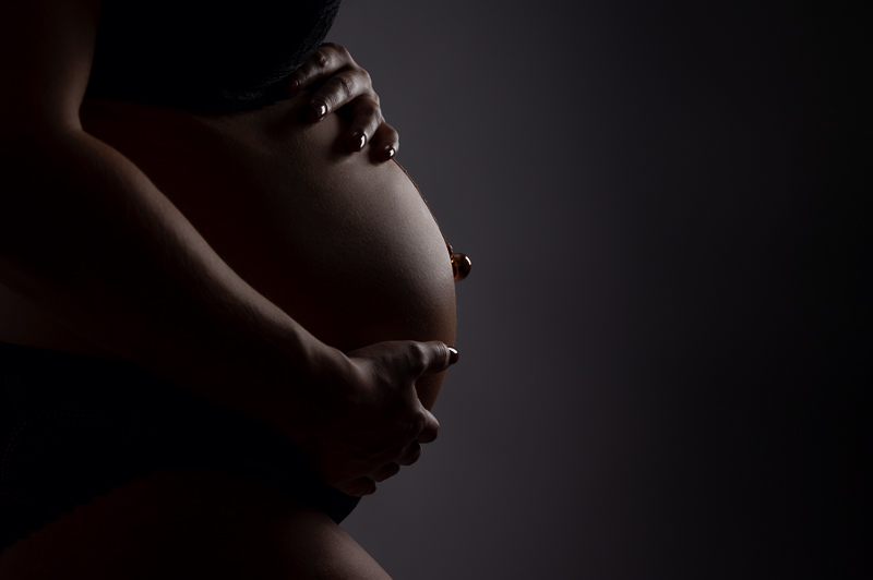 Photo de grossesse réalisée par Céline Gardé et représentant un joli ventre rond en gros plan sur fond noir.