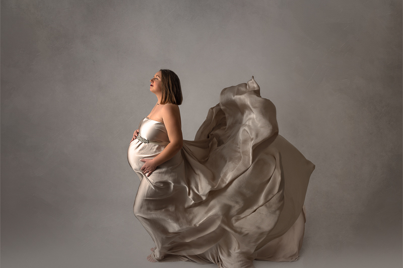 Photo de grossesse sur fond noir. Elle représente le couple de futurs parents dans les bras l'un de l'autre et les mains posées sur le ventre.