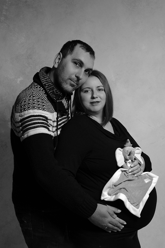 Photo de grossesse sur fond noir. Elle représente le couple de futurs parents dans les bras l'un de l'autre et les mains posées sur le ventre.