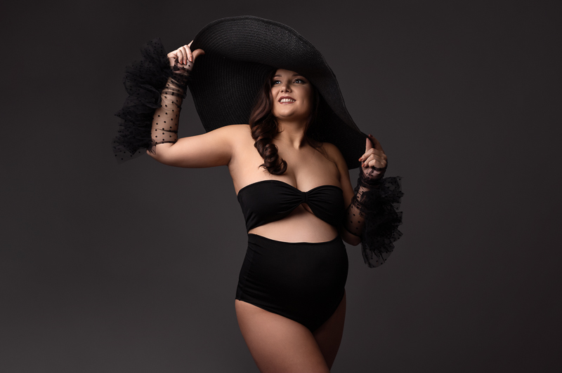 Photo de femme enceinte style mode artistique en studio à aubig Photo grossesse en studio avec grand chapeau noir et gants à plumetis – ambiance élégante