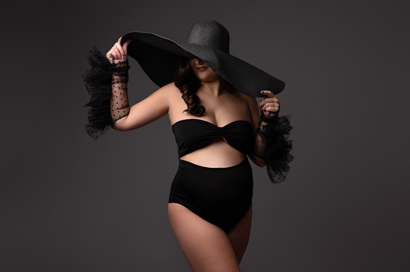 photographe de femme enceinte en studio à aubigny les clouzeaux Photo grossesse en studio avec grand chapeau noir et gants à plumetis – ambiance élégante