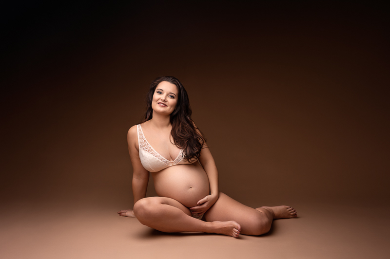 Photographe grossesse artistique et mode en studio à aubigny le Femme enceinte souriante assise au sol lors d’un shooting grossesse en studio à La Roche-sur-Yon