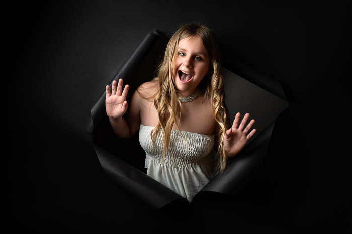 Portrait d’adolescente souriante perçant un fond noir au studio Céline Gardé Photographe à Aubigny-Les-Clouzeaux, près de La Roche-sur-Yon.