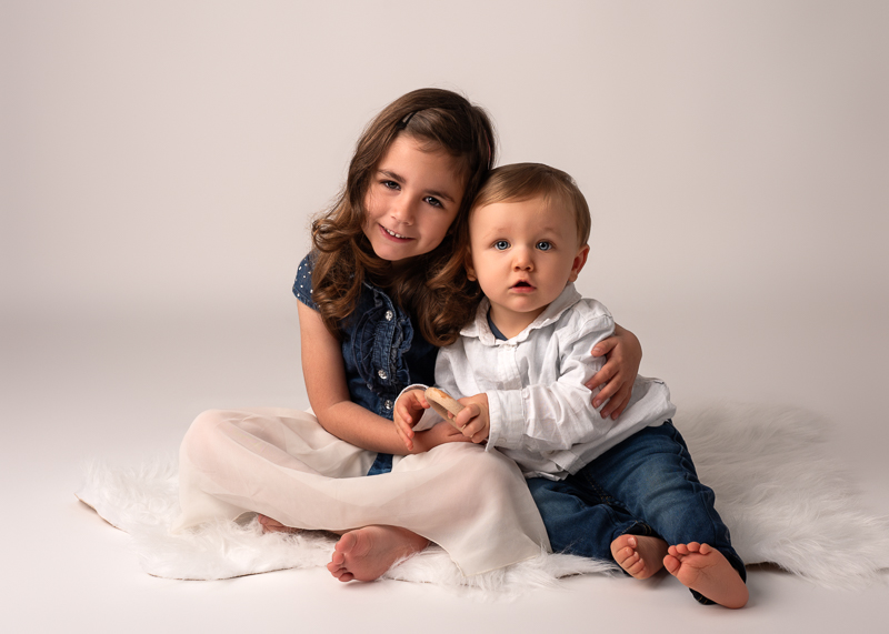 photo-fratrie-bebe-et-enfant-studio Séance photo entre cousins avec une grande fille et un bébé assis côte à côte en studio.