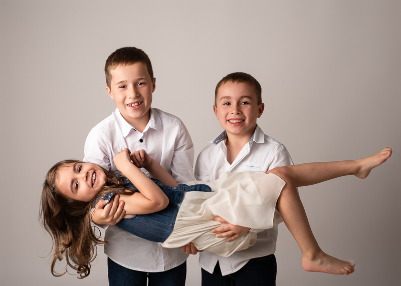 seance-photo-cousins-studio-enfants-complicite-vendee Séance photo entre cousins en studio montrant deux garçons portant leur cousine avec complicité.
