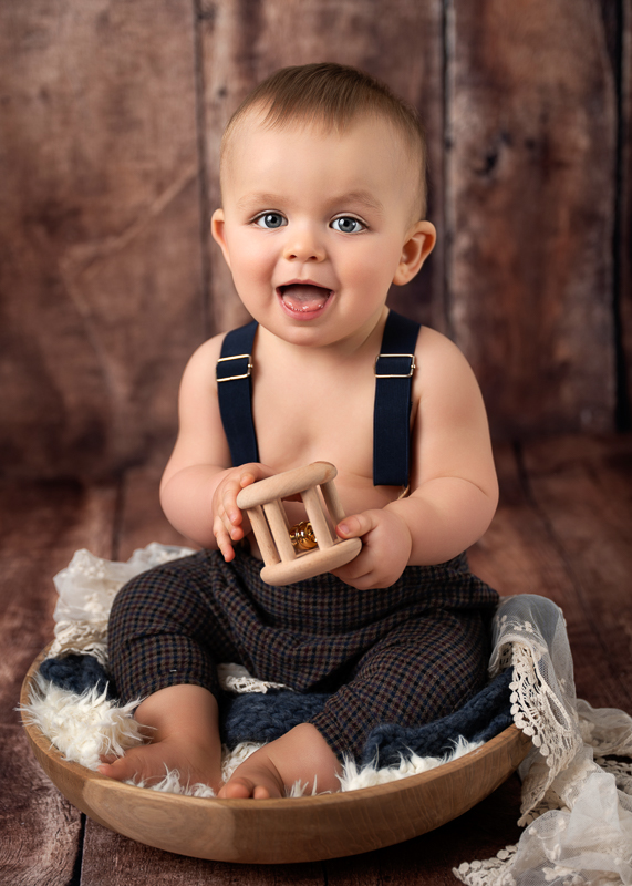 Bébé de 9 mois souriant tenant un jouet en bois lors d’une séance photo bébé au studio de Céline Gardé photographe près de La Roche-sur-Yon et Saint-Vincent-Sterlanges en Vendée
