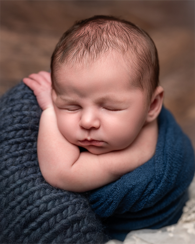 Bébé endormi posé sur une grosse maille bleue, joues contre ses bras, séance naissance en studio