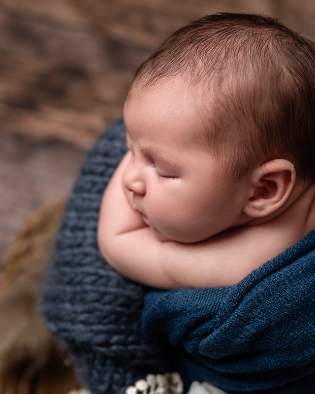Bébé endormi posé sur une grosse maille bleue, joues contre ses bras, séance naissance en studio
