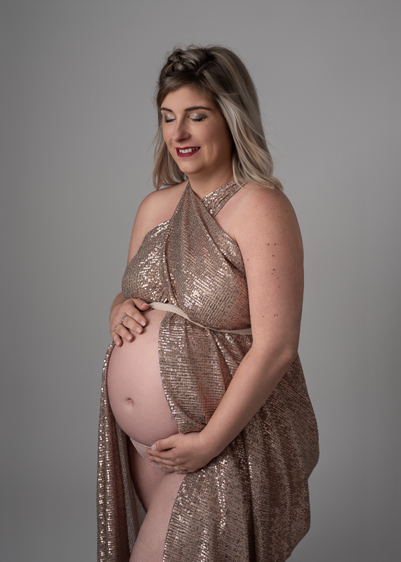 Séance photo grossesse Vendée – Robe pailletée dorée Femme enceinte en robe pailletée dorée regardant son ventre, séance photo grossesse en studio en Vendée