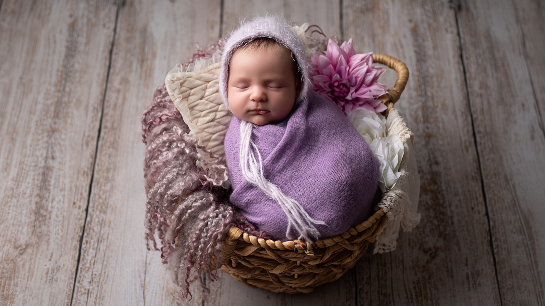 Photo d'un bébé de 7 jours, confortablement installé dans un panier en osier, avec une jolie couverture. Un décor tout doux pour ses premiers souvenirs.
